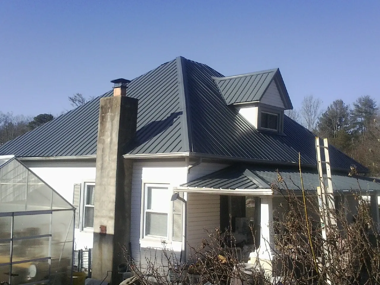 Dark blue standing seam metal roof on a white farmhouse with dormer — Slate & Tile Roof Repair by Roofing Brothers in Friedens