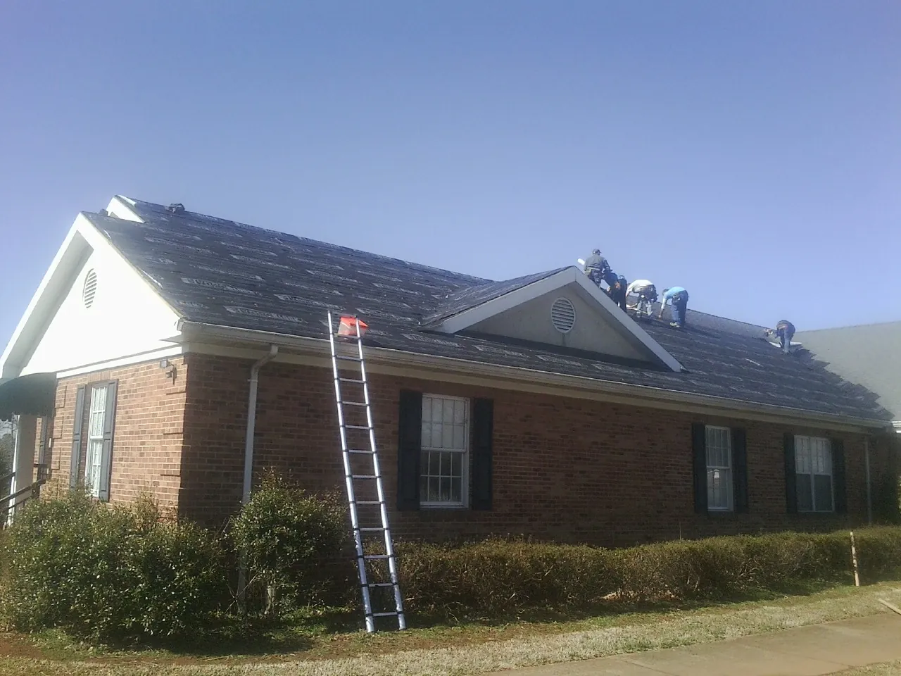 Crew tearing shingles off a brick ranch roof with a ladder set — Emergency Roof Repair work by our crew in Friedens