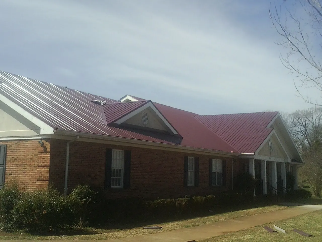 Red metal roof with gabled entries on a long brick building, from a Hail Damage Roof Repair job in Friedens