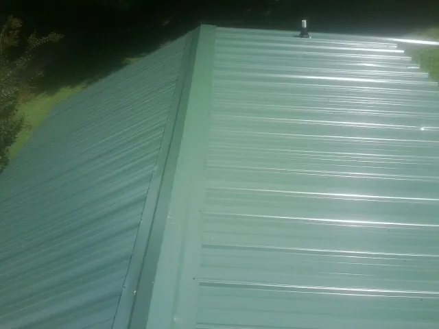 New green metal panels meeting at the ridge of a roof — Flat Roof Repair work by our crew in Friedens
