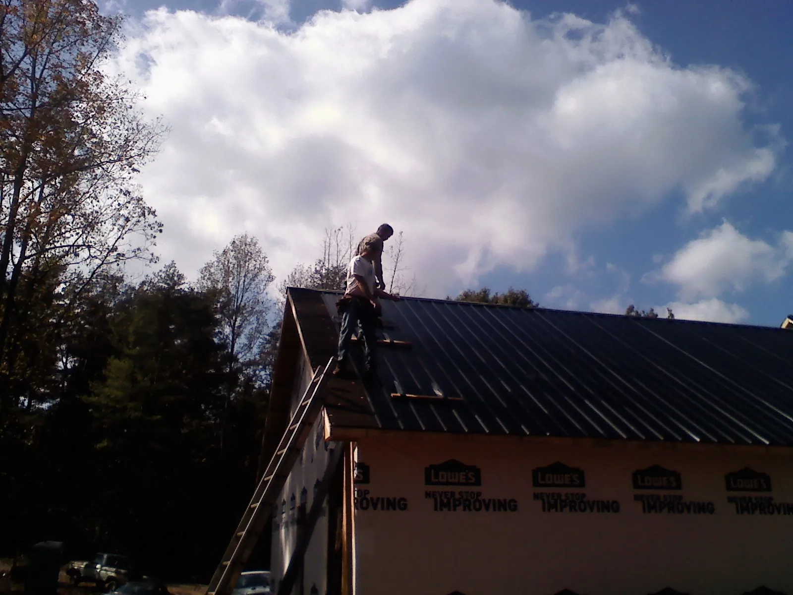Roofer fastening dark metal panels high against a cloudy sky, from a Roof Inspection job in Friedens